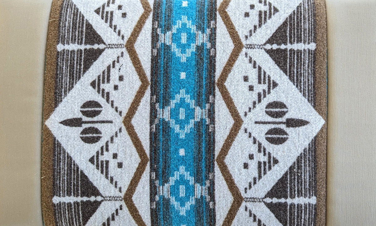 A close-up of a woven textile with a Southwestern geometric pattern, featuring a central turquoise blue stripe flanked by white and brown diamond motifs.