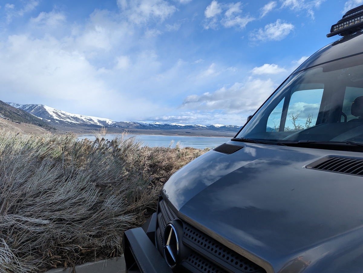 Gray van parked in a scenic location with mountains and lake in the background