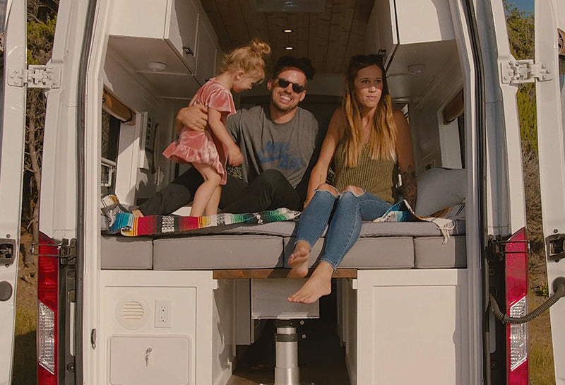 Family inside a van with the back door open, surrounded by nature.