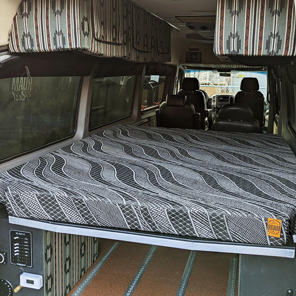 A custom camper bed setup inside a van, featuring a raised platform with a RoamRest mattress 