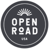 A circular dark gray logo with white text reading 'OPEN ROAD USA' and a white sunburst icon above, on a white background.